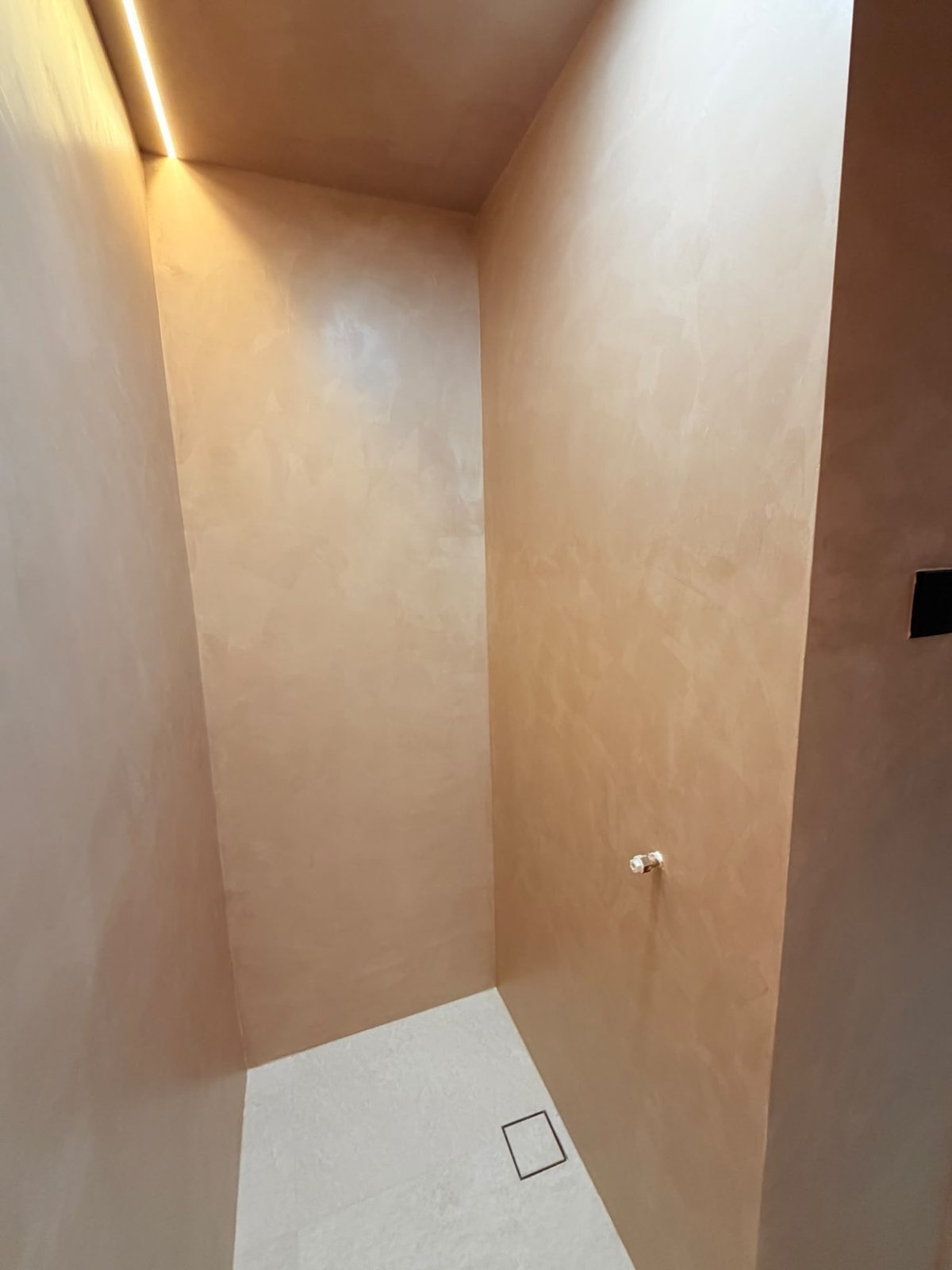 Warm-toned microcement walls in a shower with a cove light